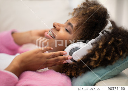 Joyful young black woman listening to music, using wireless headphones Joyful young black woman listening to music, using wireless headphones 98573460