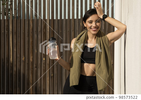 Glad muscular slim young european woman athlete in sportswear with towel and bottle of water relaxing 98573522