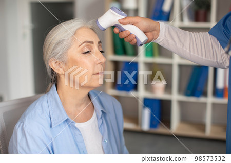 Doctor measures temperature with non-contact thermometer of old caucasian lady patient in clinic Doctor measures temperature with non-contact thermometer of old caucasian lady patient in clinic 98573532