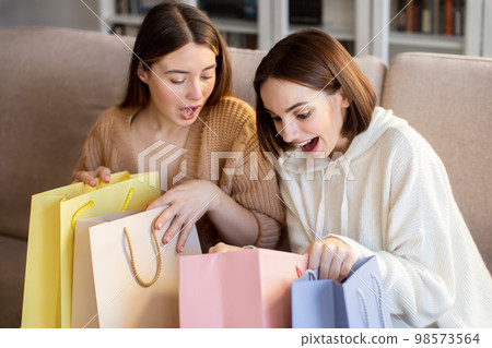 Happy surprised european millennial girlfriends shopaholic in sweaters open bags from store, enjoy free time 98573564