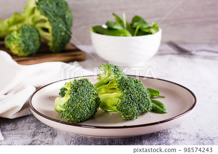 Fresh broccoli divided into inflorescences on a plate on the table. Vegetable diet. Fresh broccoli divided into inflorescences on a plate on the table. Vegetable diet. 98574243
