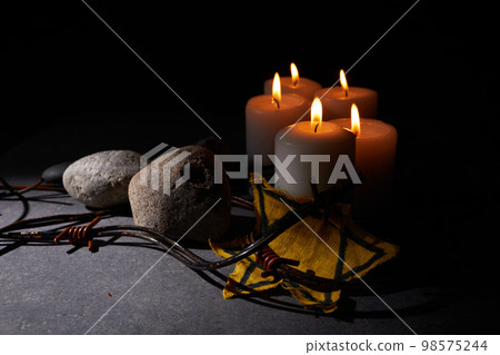 Holocaust memory day. Barbed wire, stones, yellow star and burning candle on black background 98575244