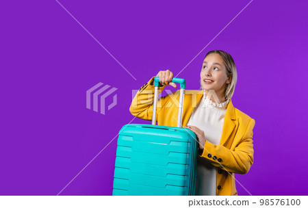 Pretty woman with carry-on suitcase on violet background. Teenager traveling. 98576100