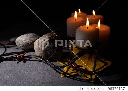 Holocaust memory day. Barbed wire, stones, yellow star and burning candle on black background 98576137