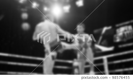 Blurred images black and white photo style of Thai boxing or Muay Thai or Kickboxing which local and foriegn boxer are fighting on the ring at indoor stage as martial art sport. Muay Thai Kick boxing 98576455