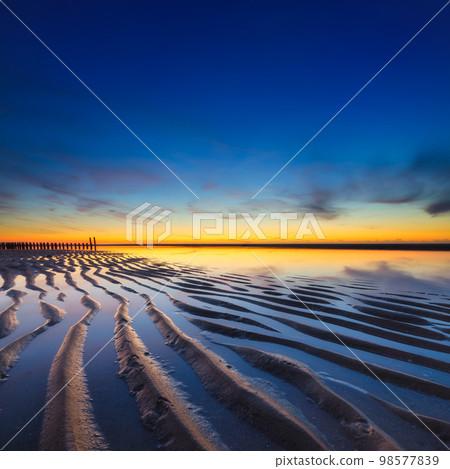 A seascape during sunset. Lines of sand on the seashore. Bright sky during sunset. 98577839