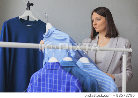 woman takes hangers with clothes, blue jacket shirt wardrobe. storing clothes or shopping. woman takes hangers with clothes, blue jacket shirt wardrobe. storing clothes or shopping. 98578796