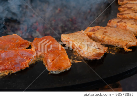 Process of cooking meat steaks on round brazier - close up Process of cooking meat steaks on round brazier - close up 98578885