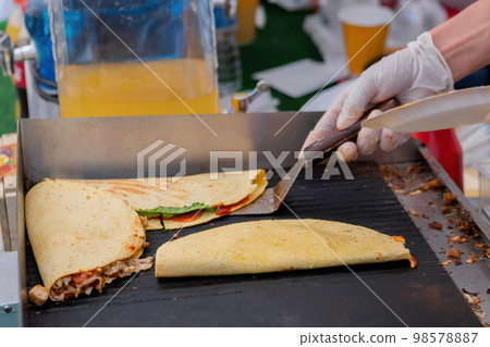 Chef preparing fresh quesadilla on black grill at summer local food market Chef preparing fresh quesadilla on black grill at summer local food market 98578887