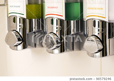 Fragment of body wash liquid soap, shampoo and conditioner dispensers on hotel bathroom shower wall 98579246