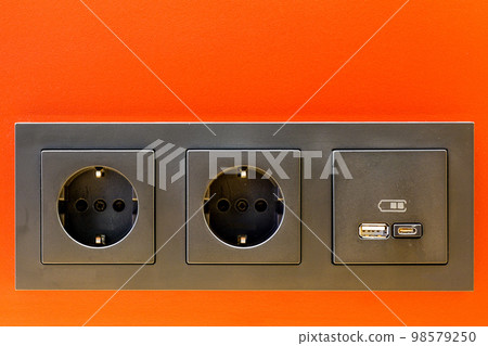 A black 220V, USB and USB C socket block is built into the orange wall surface A black 220V, USB and USB C socket block is built into the orange wall surface 98579250