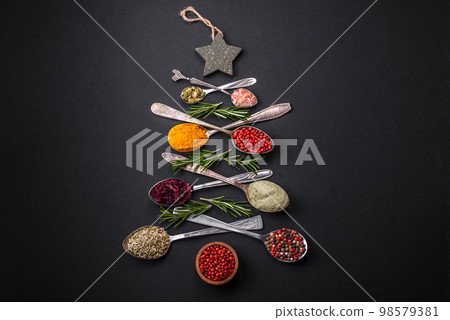 Composition consisting of a variation of spices in metal spoons laid out in the shape of a Christmas tree 98579381