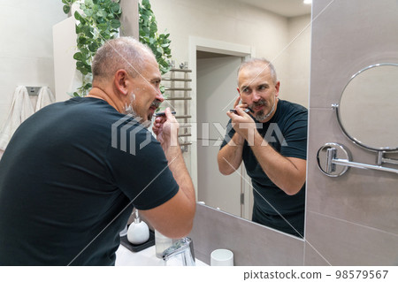 Middle aged handsome man shaving his beard in bathroom Middle aged handsome man shaving his beard in bathroom 98579567
