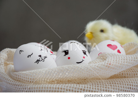Easter eggs lie in mesh bag. Yellow chick sits on eggs on dark background. Funny peaks and twig with red flowers are drawn. Copy space. Happy Easter Easter eggs lie in mesh bag. Yellow chick sits on eggs on dark background. Funny peaks and twig with red flowers are drawn. Copy space. Happy Easter 98580370