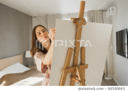 Young woman artist painting on canvas on the easel at home in bedroom - art and creativity concept 98580663