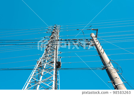 Power transmission towers supporting electric wires and high-voltage transmission lines in a residential area and a clear sky light tone Power transmission towers supporting electric wires and high-voltage transmission lines in a residential area and a clear sky light tone 98583263