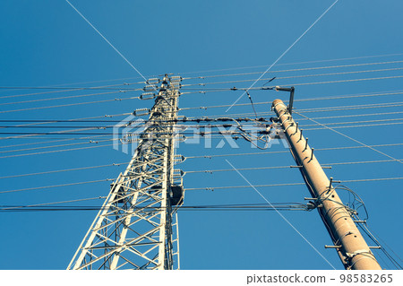 Power transmission towers that support electric wires and high-voltage transmission lines in a residential area, and a sunny sky, emphasized in warm colors Power transmission towers that support electric wires and high-voltage transmission lines in a residential area, and a sunny sky, emphasized in warm colors 98583265