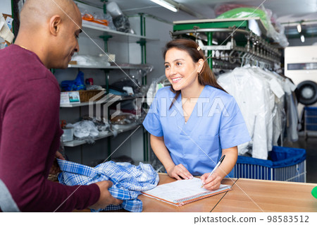 Woman dry-cleaning worker receiving clothes from client Woman dry-cleaning worker receiving clothes from client 98583512