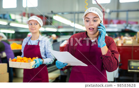 Positive cheerful woman worker conducts business negotiations on the phone on fruit processing plant. 98583628