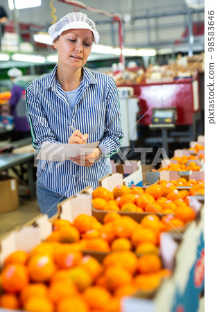Positive female worker fills out a document at a citrus processing plant. 98583646