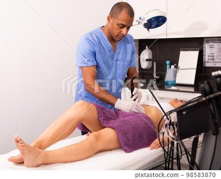 Cosmetologist performing ultrasound cavitation body procedure for female client 98583870