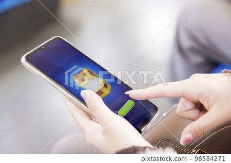 在火車上用智能手機遊戲充電並玩Gacha的年輕女性的手 在火車上用智能手機遊戲充電並玩Gacha的年輕女性的手 98584271