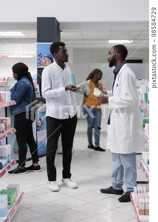 African american customers purchasing medicaments in pharmacy store, pharmacist recommending man vitamin c in drugstore, woman buying prescription treatment, all black team 98584729