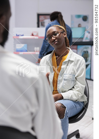 Pharmacy consultation, african american customer talking with pharmacist, sitting in drugstore. Client and chemist communication, pharmaceutical service, medical check up Pharmacy consultation, african american customer talking with pharmacist, sitting in drugstore. Client and chemist communication, pharmaceutical service, medical check up 98584732