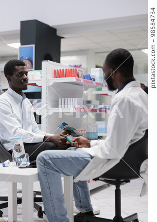 African american pharmacist measuring patient blood sugar with glucometer, pharmacy professional consultation. Glucose level measurement in drugstore, diabetes diagnosis, all black team African american pharmacist measuring patient blood sugar with glucometer, pharmacy professional consultation. Glucose level measurement in drugstore, diabetes diagnosis, all black team 98584734