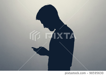 Male silhouette looking at screen of smart phone Male silhouette looking at screen of smart phone 98595630