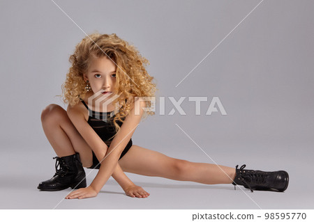 Beautiful little girl gymnast in a black sports swimsuit and boots on a gray background. Beautiful little girl gymnast in a black sports swimsuit and boots on a gray background. 98595770
