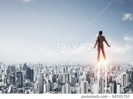 Businessman in suit and aviator hat flying in sky 98595783