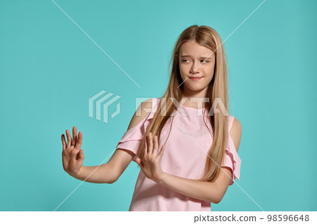 Studio portrait of a beautiful girl blonde teenager in a pink t-shirt posing over a blue background. 98596648