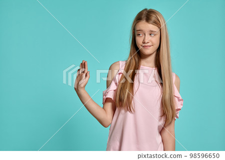 Studio portrait of a beautiful girl blonde teenager in a pink t-shirt posing over a blue background. 98596650
