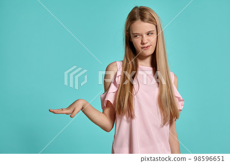 Studio portrait of a beautiful girl blonde teenager in a pink t-shirt posing over a blue background. Studio portrait of a beautiful girl blonde teenager in a pink t-shirt posing over a blue background. 98596651