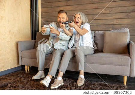 Mature couple playing video games and looking excited Mature couple playing video games and looking excited 98597363