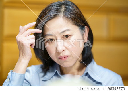 Middle-aged woman looking in the mirror and touching her gray hair Middle-aged woman looking in the mirror and touching her gray hair 98597773