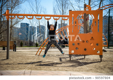 Cute boy is climbing on the playground in the schoolyard. He has a very happy face and enjoy this adventure sports alone outdoor. Warm sunny day 98597804