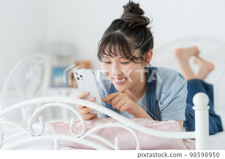 Z generation girl lying on the bed and operating a smartphone Z generation girl lying on the bed and operating a smartphone 98598950