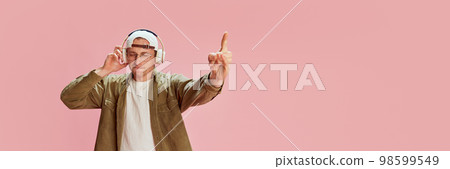 Young emotive man in casual clothes emotionally listening to music in headphones, posing over pink studio background. Concept of emotions, lifestyle Young emotive man in casual clothes emotionally listening to music in headphones, posing over pink studio background. Concept of emotions, lifestyle 98599549