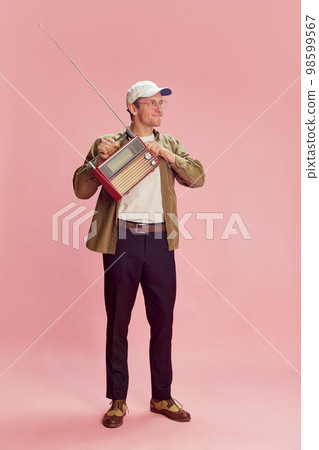 Listening to music, news. Young positive man posing with retro radio set over pink studio background. Concept of emotions, lifestyle 98599567