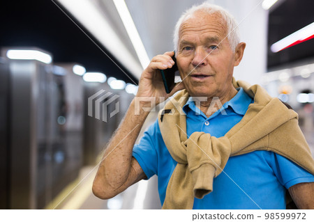 Elderly man using mobile phone while waiting for train in platform of underground station Elderly man using mobile phone while waiting for train in platform of underground station 98599972