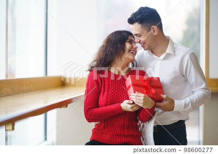Man gives to his woman a gift box with red ribbon. A loving couple celebrating Valentine's Day. 98600277