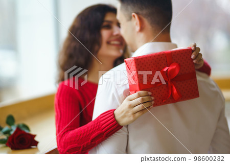 Man gives to his woman a gift box with red ribbon. A loving couple celebrating Valentine's Day. Man gives to his woman a gift box with red ribbon. A loving couple celebrating Valentine's Day. 98600282