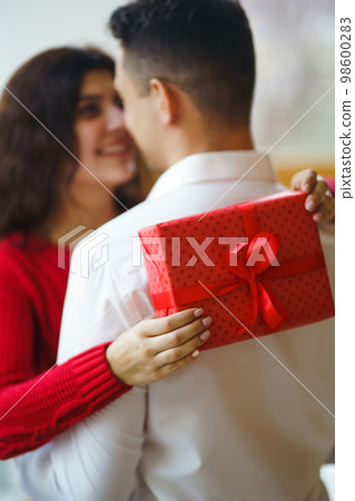 Man gives to his woman a gift box with red ribbon. A loving couple celebrating Valentine's Day. Man gives to his woman a gift box with red ribbon. A loving couple celebrating Valentine's Day. 98600283