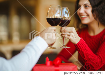 Couple clink glasses with red wine. Lovers give each other gifts. Lovely romantic dinner. 98600299