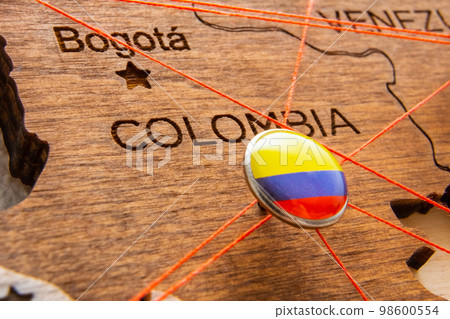 Colombia flag on the pushpin with red thread showed the paths of movement or areas of influence in the global economy on the wooden map. Planning of traveling or logistic concept. Network connection.  98600554