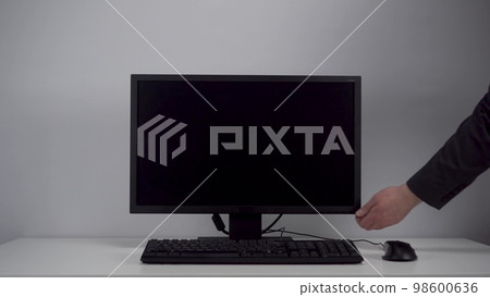 Turning on the monitor with a green screen. A man with his hand turns on the computer screen on the desktop in the office. Chroma key. 98600636