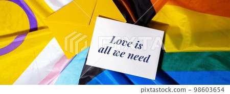LOVE IS ALL WE NEED text on valentine card inscription positive quote phrase Greeting card on Rainbow LGBTQIA flag made from silk material. Symbol of LGBTQ pride month. Equal rights. Peace and 98603654