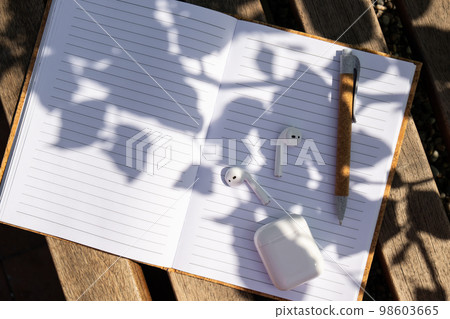 Paper notebook with wireless headphones. Mockup Coffee break. Audio healing, sound therapy wellness rituals, positive mental health habits listening podcast writing self discovery gratitude journal. 98603665